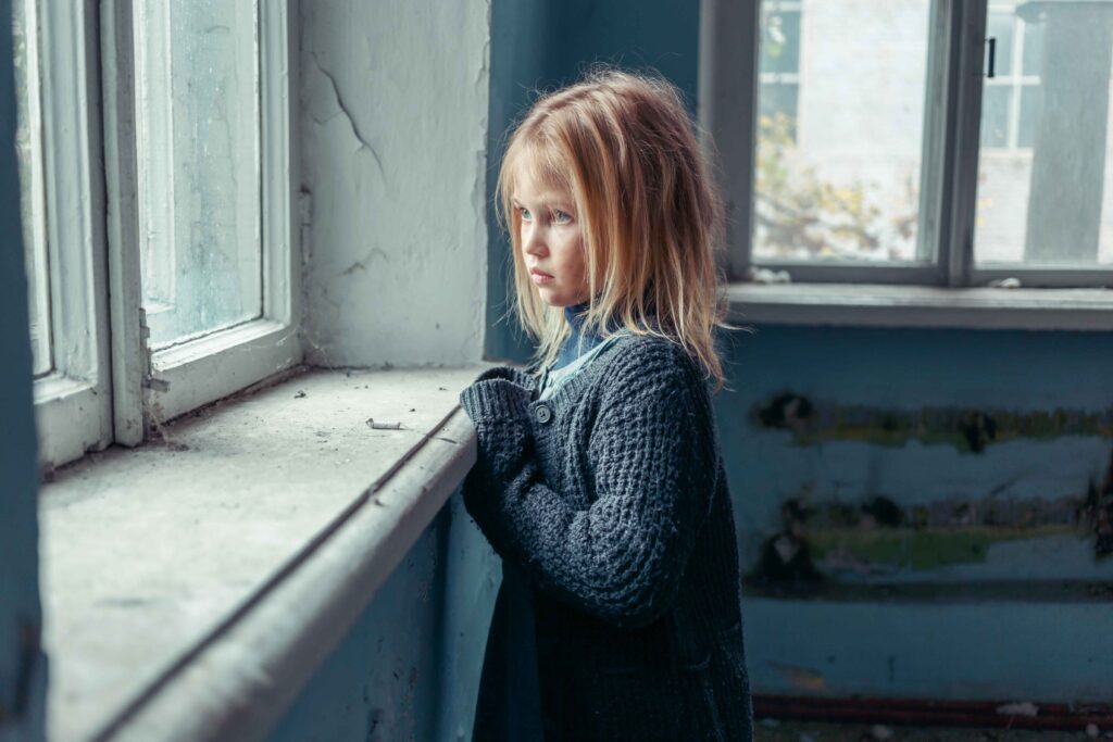 Depressed poor girl standing near window